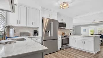 A modern kitchen with white cabinetry, stainless steel appliances, a marble countertop, and a wooden floor.