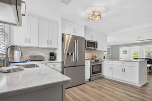 Una cocina moderna con armarios blancos, electrodomésticos de acero inoxidable, encimera de mármol y suelo de madera.