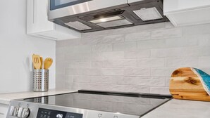 Una cocina moderna con una placa de inducción de acero inoxidable, horno empotrado y salpicadero de azulejos blancos.
