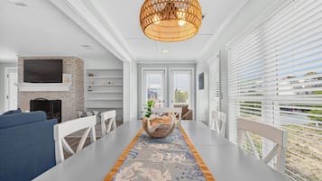 A modern living room with a dining area, a fireplace, and a large window with blinds.