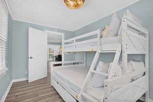 Habitación con literas, una puerta, una ventana con persianas y una lámpara colgante.