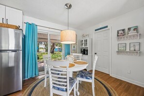 Eine Küche mit Kühlschrank, einem Esstisch mit Stühlen, einer Hängelampe und Blick ins Freie.