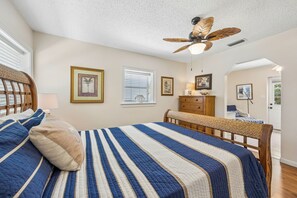 Ein Schlafzimmer mit einem Bett, einer hölzernen Bank, einem Deckenventilator und gerahmten Kunstwerken an den Wänden.