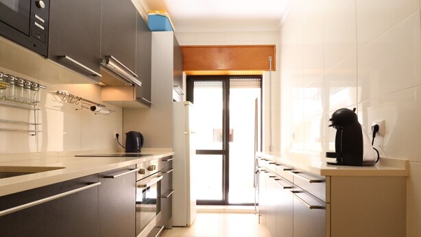 A modern kitchen with stainless steel appliances, a coffee machine, and a view through a glass door. - MyStay - Apartment in Alvor with a pool (Alvor)