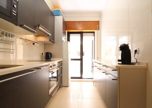 A modern kitchen with stainless steel appliances, a coffee machine, and a view through a glass door. - MyStay - Apartment in Alvor with a pool (Alvor)
