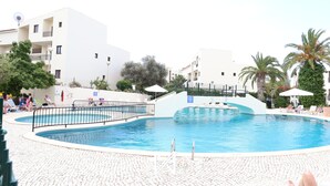 A swimming pool with a curved edge, surrounded by lounge chairs and umbrellas, with buildings in the background. - MyStay - Apartment in Alvor with a pool (Alvor)
