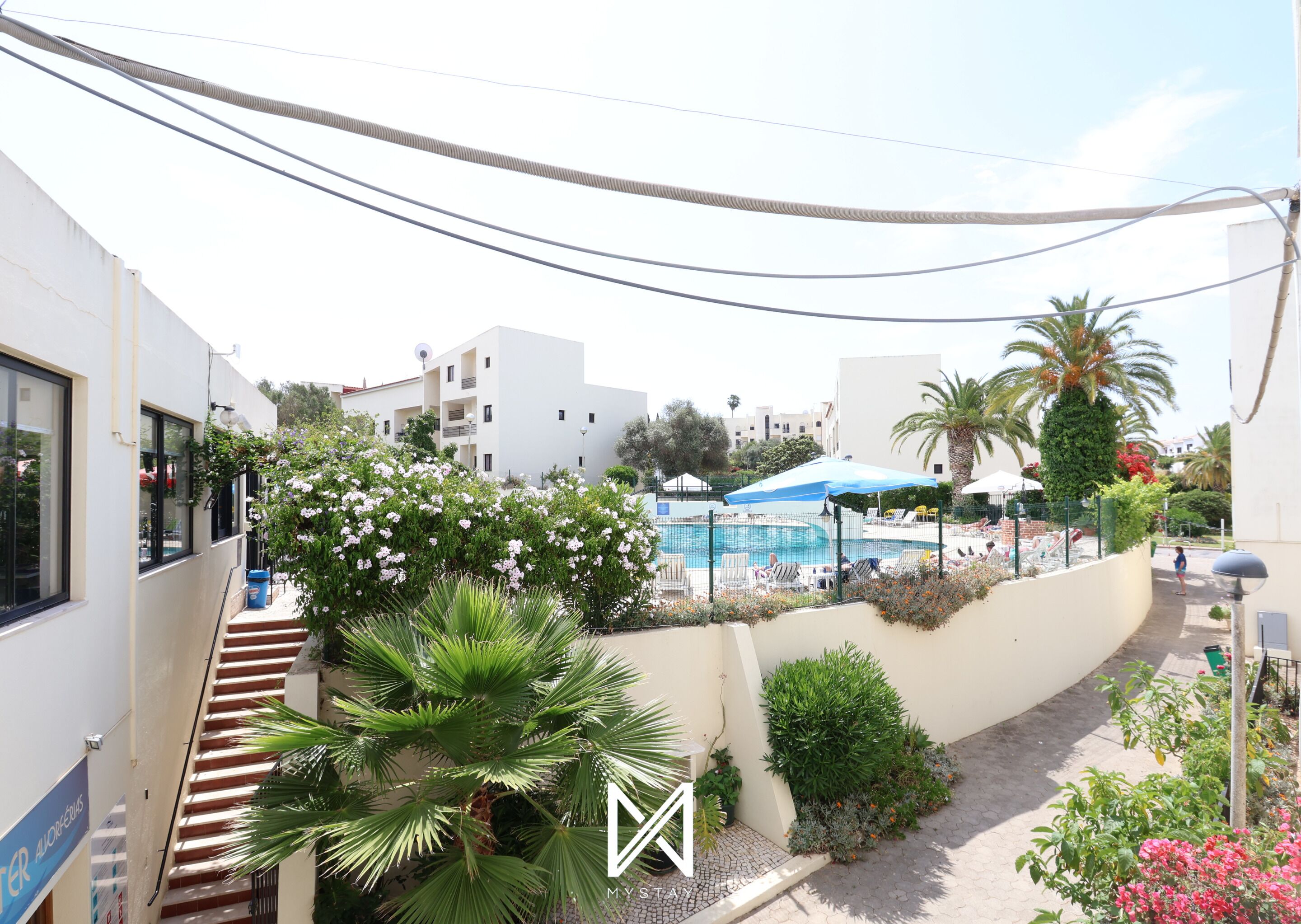 Un edificio residencial con piscina, mobiliario exterior y abundante vegetación.