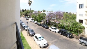 A parking lot with multiple cars and a white van, surrounded by buildings and trees with purple flowers. - MyStay - Apartment in Alvor with a pool (Alvor)