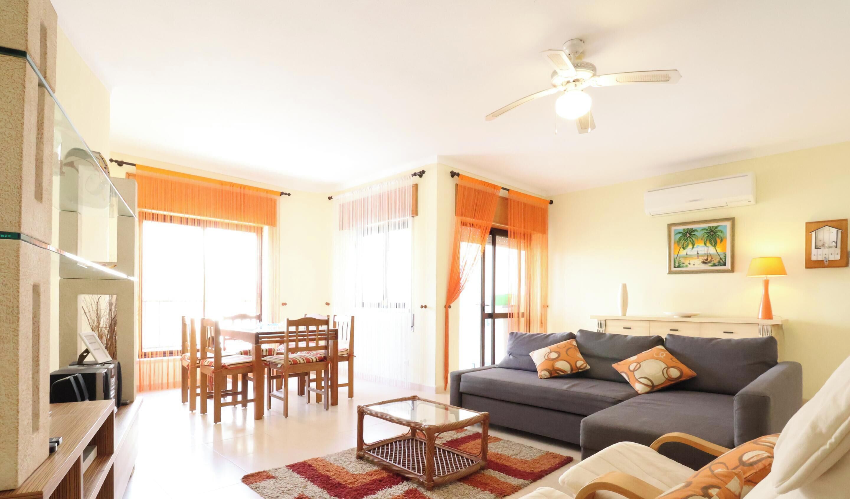 A living room with a sofa, coffee table, dining table with chairs, and a ceiling fan.