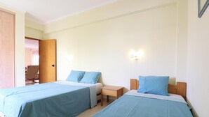 A hotel room with two beds, a wooden nightstand, and a door leading to another room. - MyStay - Apartment in Alvor with a pool (Alvor)