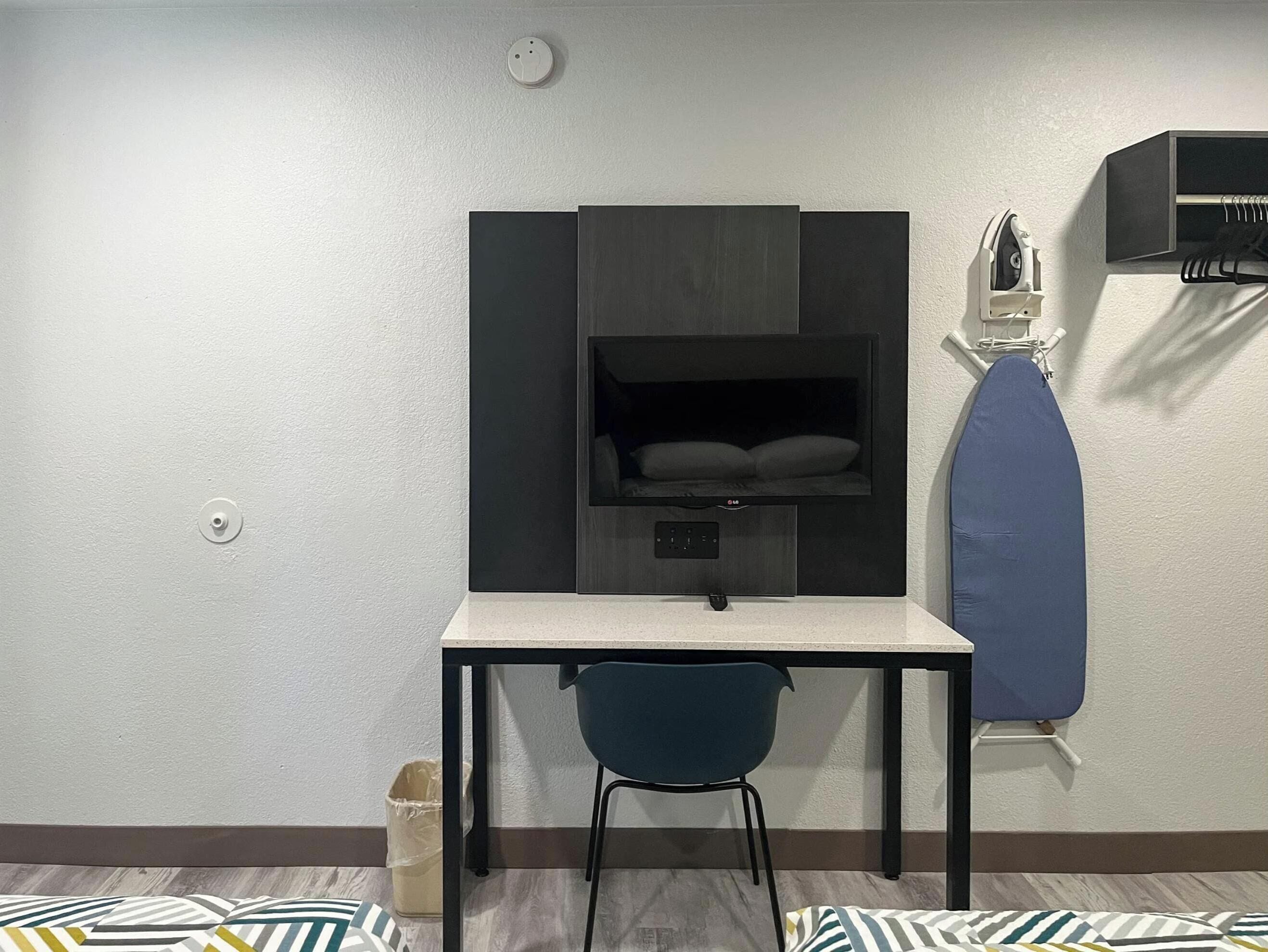 A compact room with a desk, a chair, a built-in shelf with a mattress, and an ironing board.