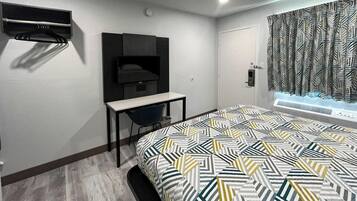 Quarto de hotel moderno com cama, escrivaninha, televisão e janela com cortinas estampadas.