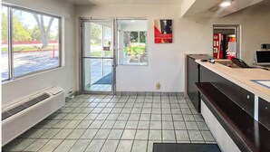 A reception area with a tiled floor, a glass door leading outside, a Coca-Cola refrigerator, and a wall-mounted sign.