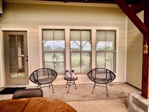 Eine überdachte Terrasse mit zwei Stühlen, einem Tisch, großen Fenstern und einer Tür.