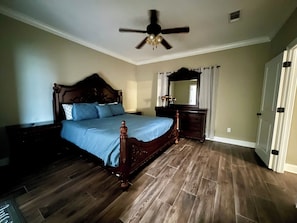 Ein Schlafzimmer mit einem hölzernen Bett, einem Deckenventilator, einem Schminktisch und einer Tür.