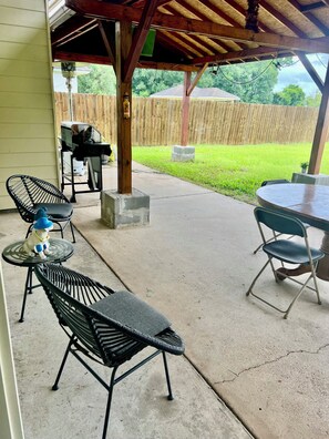 Un patio al aire libre con una parrilla, sillas y una mesa.