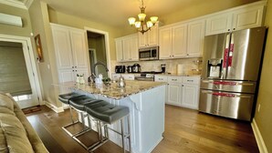 A modern kitchen with white cabinets, stainless steel appliances, and a central island with bar stools.