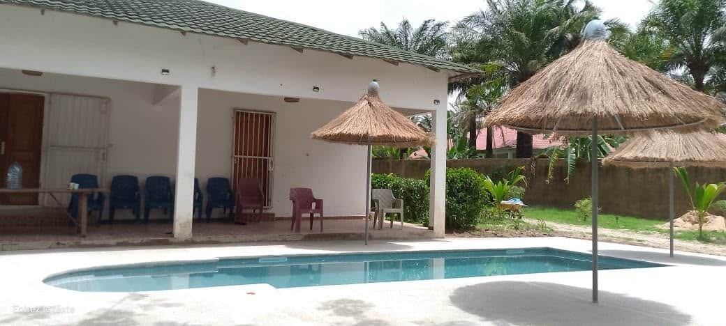 Un espace piscine avec une maison, des chaises et des parasols en chaume.