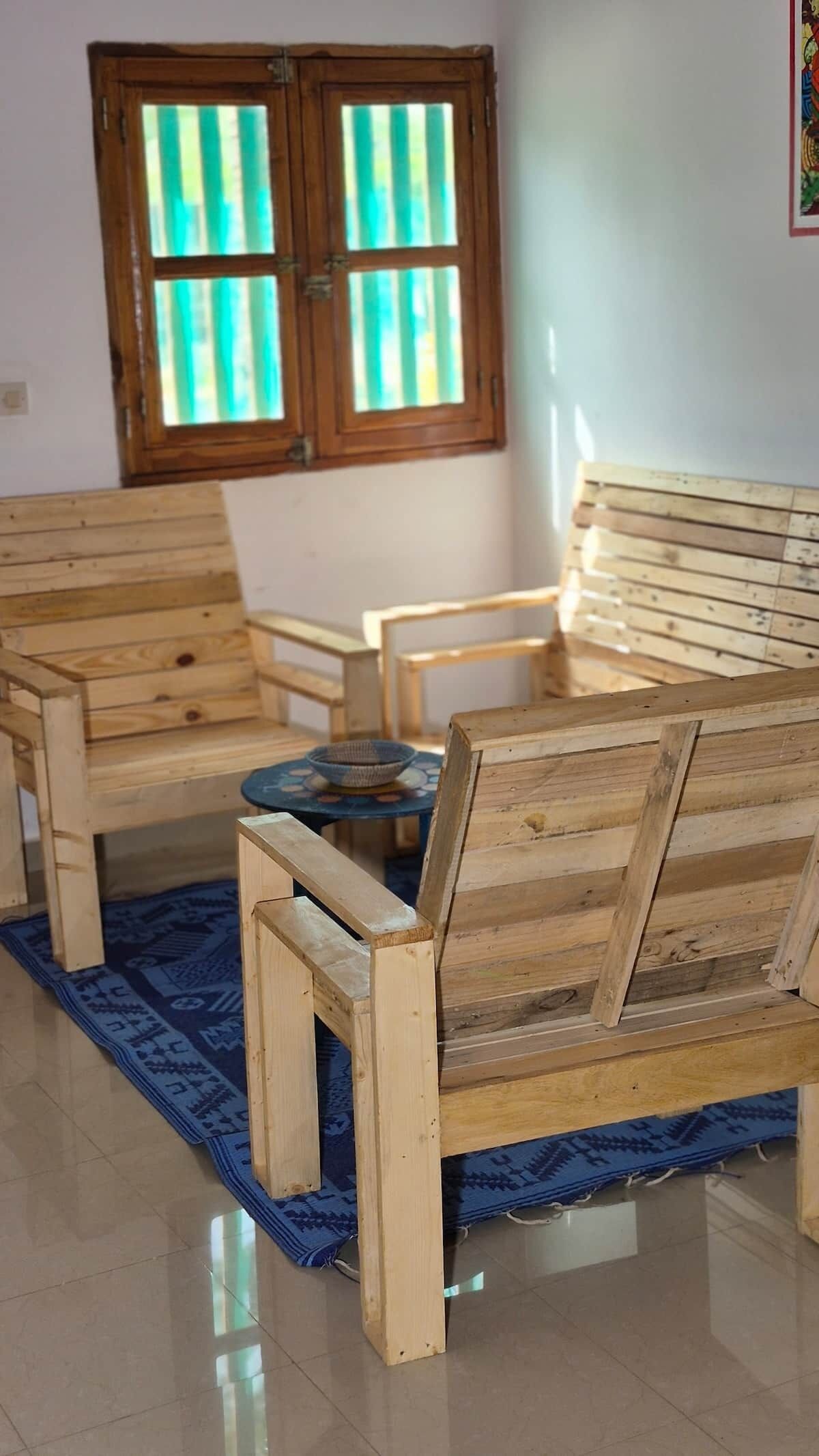 Une pièce comprenant un ensemble de meubles de salon en bois, une petite table ronde et une fenêtre avec des stores verticaux.