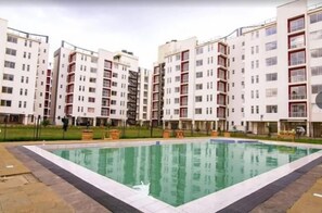 Um complexo de apartamentos moderno com uma piscina central, rodeado por edifícios de vários andares com varandas.
