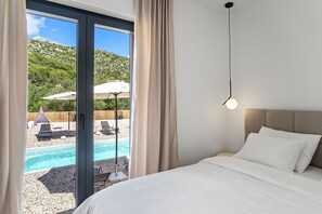 Ein Schlafzimmer mit einem Bett, Blick auf einen Pool und einem Berg im Hintergrund.