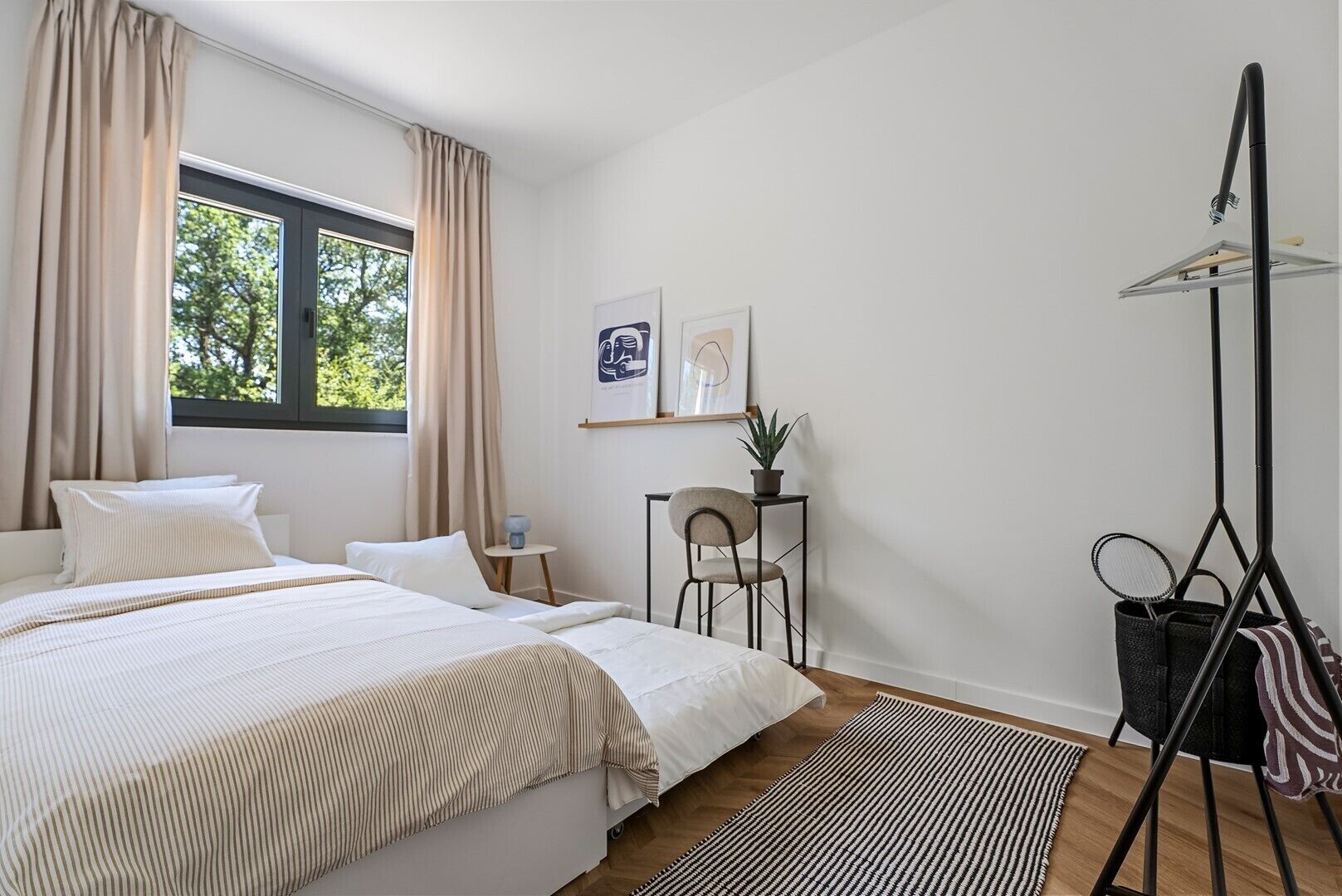 A bedroom with a bed, a chair, a small table, a potted plant, and a hanging light fixture.