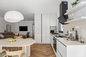 A modern kitchen with white cabinetry, a round dining table with chairs, a coffee machine, and a built-in oven. - Villa Three Olives: A Perfect Family Retreat near Omis (Naklice)