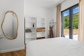 A bedroom with a bed, white shelving unit, a mirror, and a view of greenery through a window. - Villa Three Olives: A Perfect Family Retreat near Omis (Naklice)