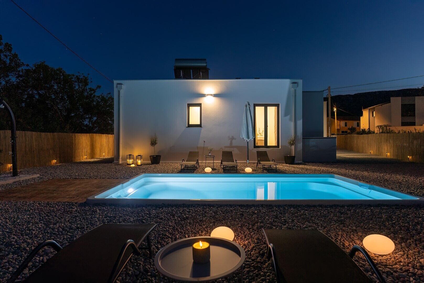 A modern outdoor pool area with lounge chairs and a candle on a table.