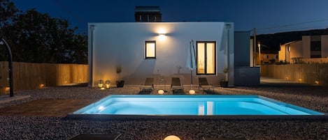 A modern outdoor pool area with lounge chairs and a candle on a table.