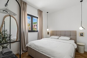 Een slaapkamer met een bed, een raam, een spiegel, een nachtkastje en een hanglamp.