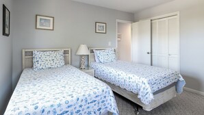 Quarto com duas camas, uma mesa de cabeceira, uma luminária e um guarda-roupa.