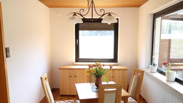 A dining area with a table, chairs, a vase with flowers, a window with blinds, and a radiator. - Charming vacation home in a stunning location right in the heart of Wingst (Wingst)