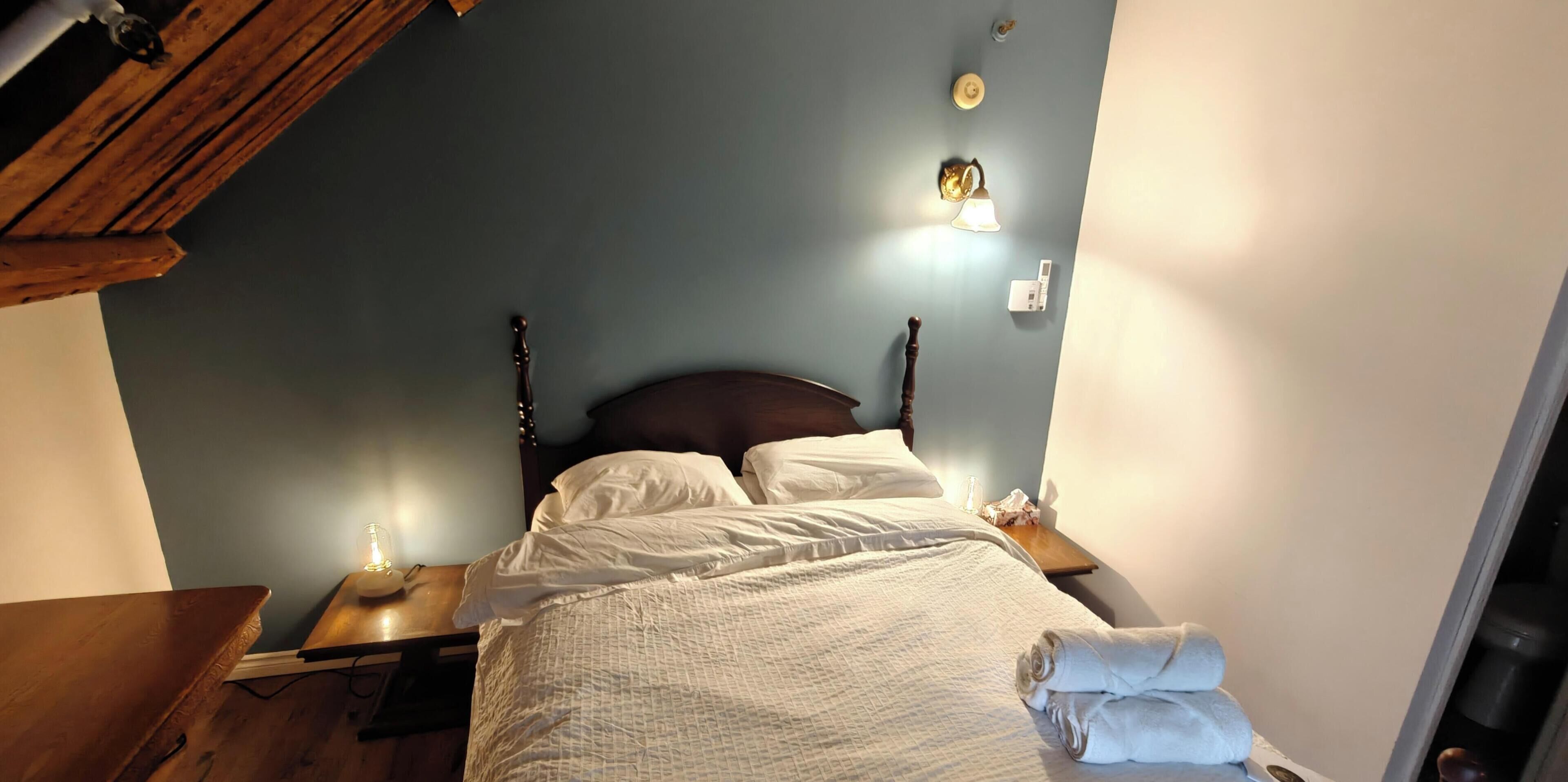 A bedroom with a bed, bedside table, lamp, and a wall-mounted light fixture.