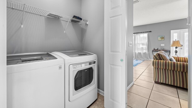 A laundry area with a dryer and a washing machine, a door leading to a living room with a sofa and a lamp. - Pet Friendly Beach House | Walk to Beach | Sleeps 6 (Panama City Beach)