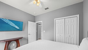 A bedroom with a bed, a TV, a ceiling fan, and a door leading to another room. - Pet Friendly Beach House | Walk to Beach | Sleeps 6 (Panama City Beach)
