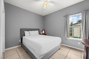 A bedroom with a bed, a nightstand, a ceiling fan, a window with curtains, and a view of the outside. - Pet Friendly Beach House | Walk to Beach | Sleeps 6 (Panama City Beach)