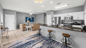 A modern kitchen with white cabinets, a stainless steel refrigerator, and a microwave. There is a dining area with a sofa and a coffee table. - Pet Friendly Beach House | Walk to Beach | Sleeps 6 (Panama City Beach)