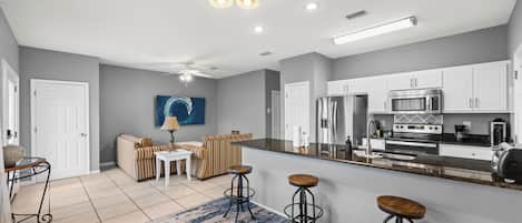 Une cuisine moderne avec des meubles blancs, un réfrigérateur en acier inoxydable et un four à micro-ondes. On y trouve également un coin repas avec un canapé et une table basse.