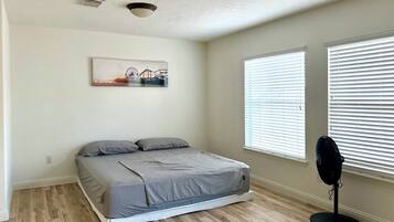 Een slaapkamer met een bed, plafondventilator en een raam met zonwering.