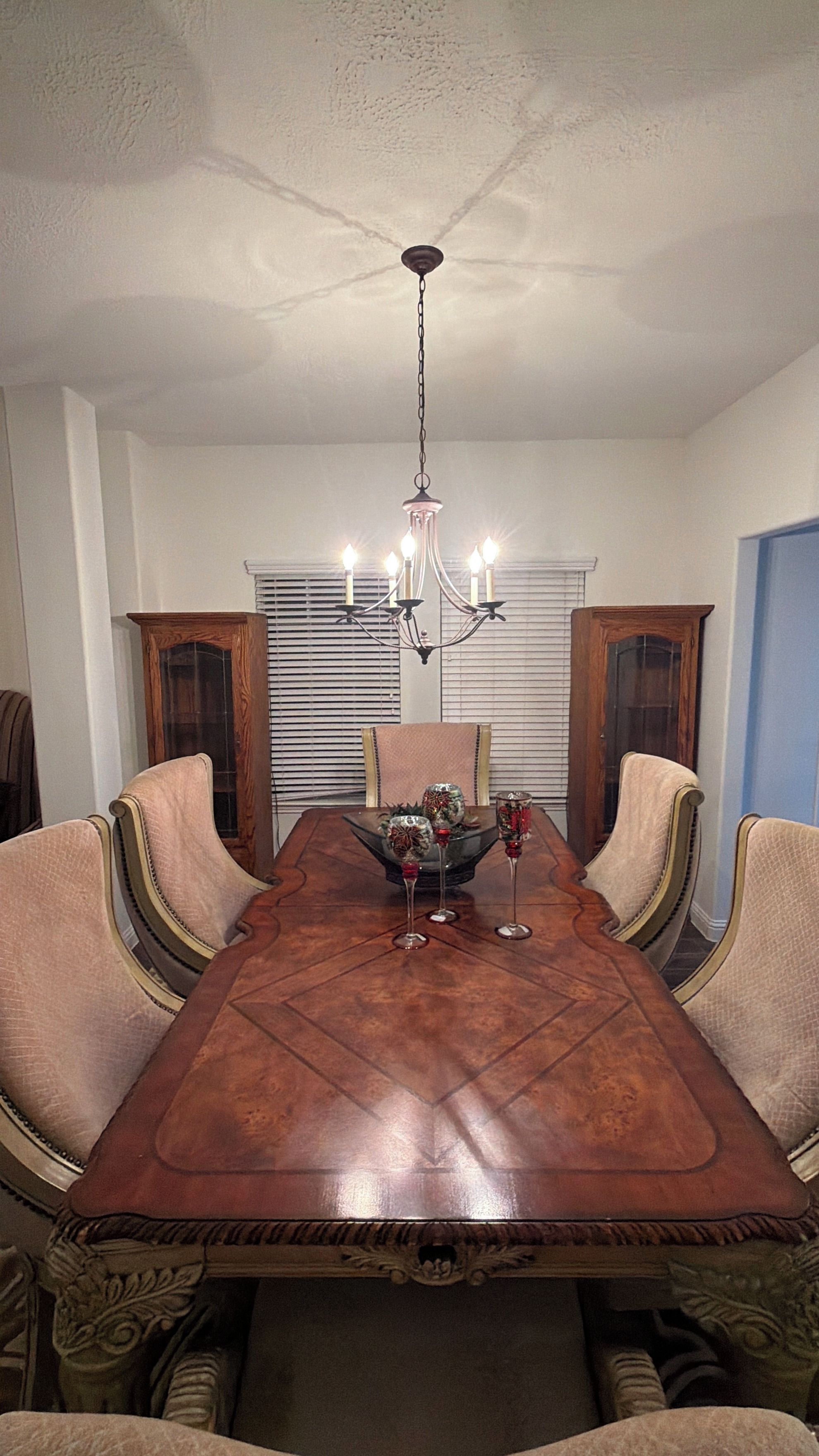 Uma sala de jantar com mesa de madeira, cadeiras, um candelabro e uma janela com persianas.