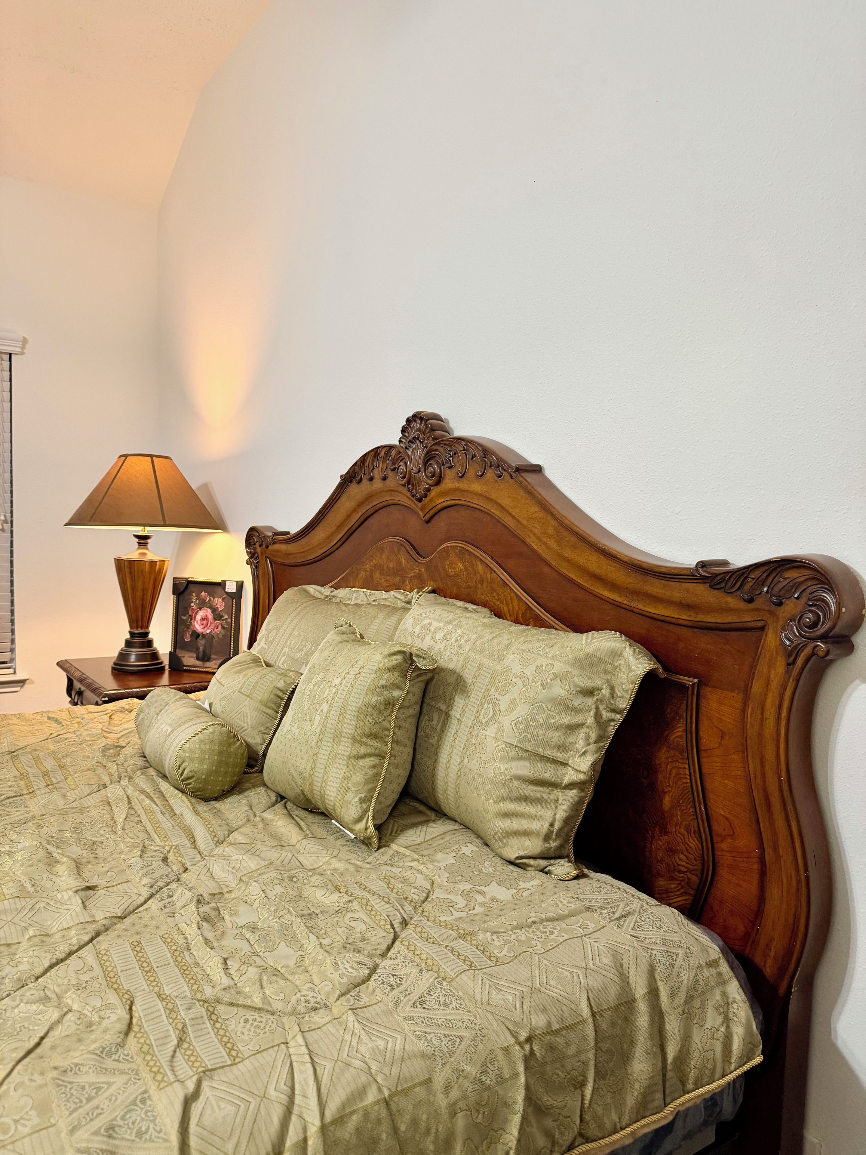 Uma cama com cabeceira de madeira, uma luminária e um quadro em uma mesinha de cabeceira.