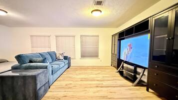 A living room with a blue sofa, a flat-screen TV on a stand, and a wooden floor.