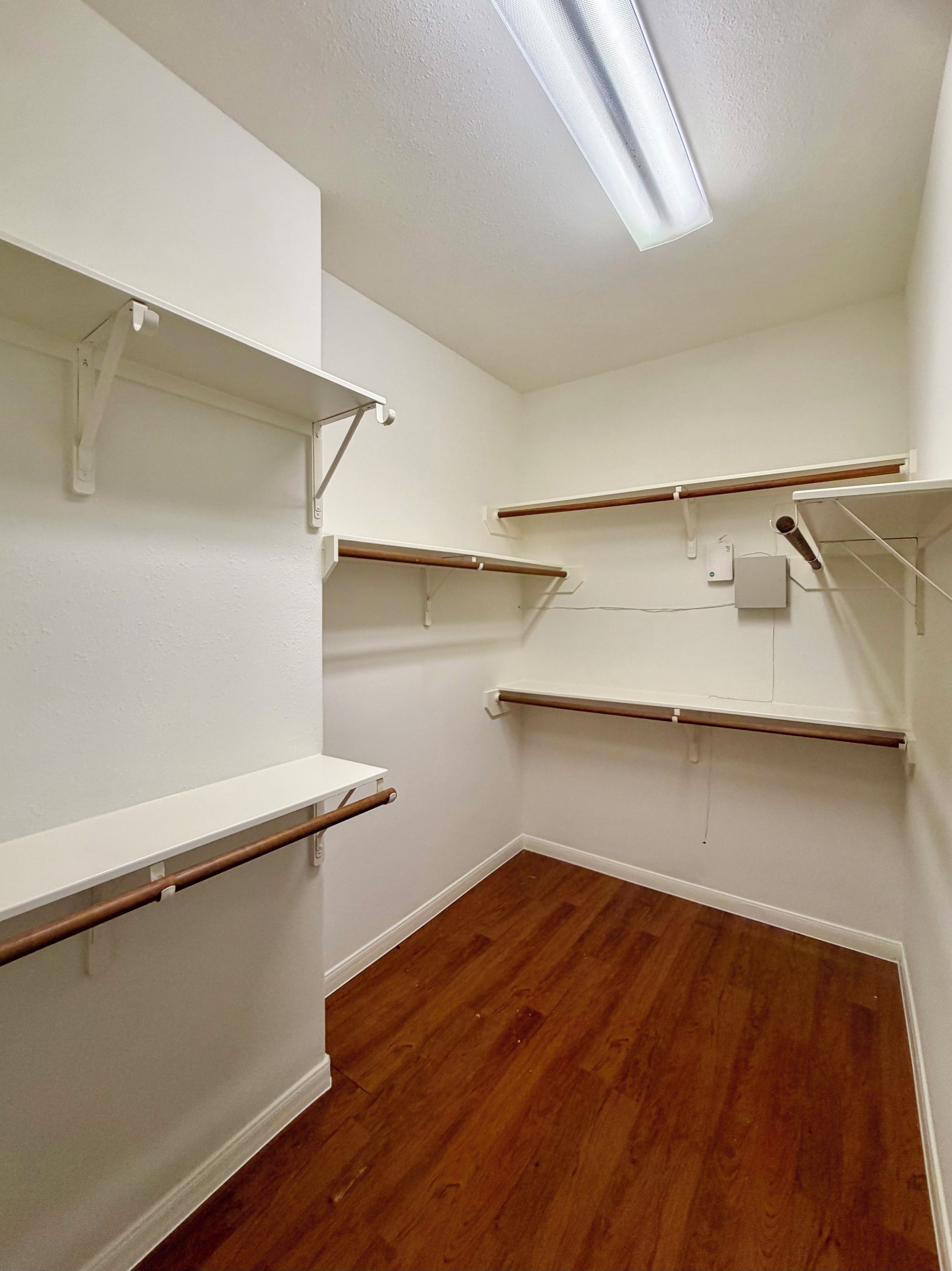 A room with white walls, wooden flooring, and multiple white shelves.