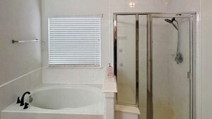 Ein Badezimmer mit Badewanne, Duschkabine und einem Fenster mit Jalousien.