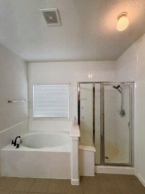 Une salle de bain avec une baignoire, un espace douche et une fenêtre avec des stores.
