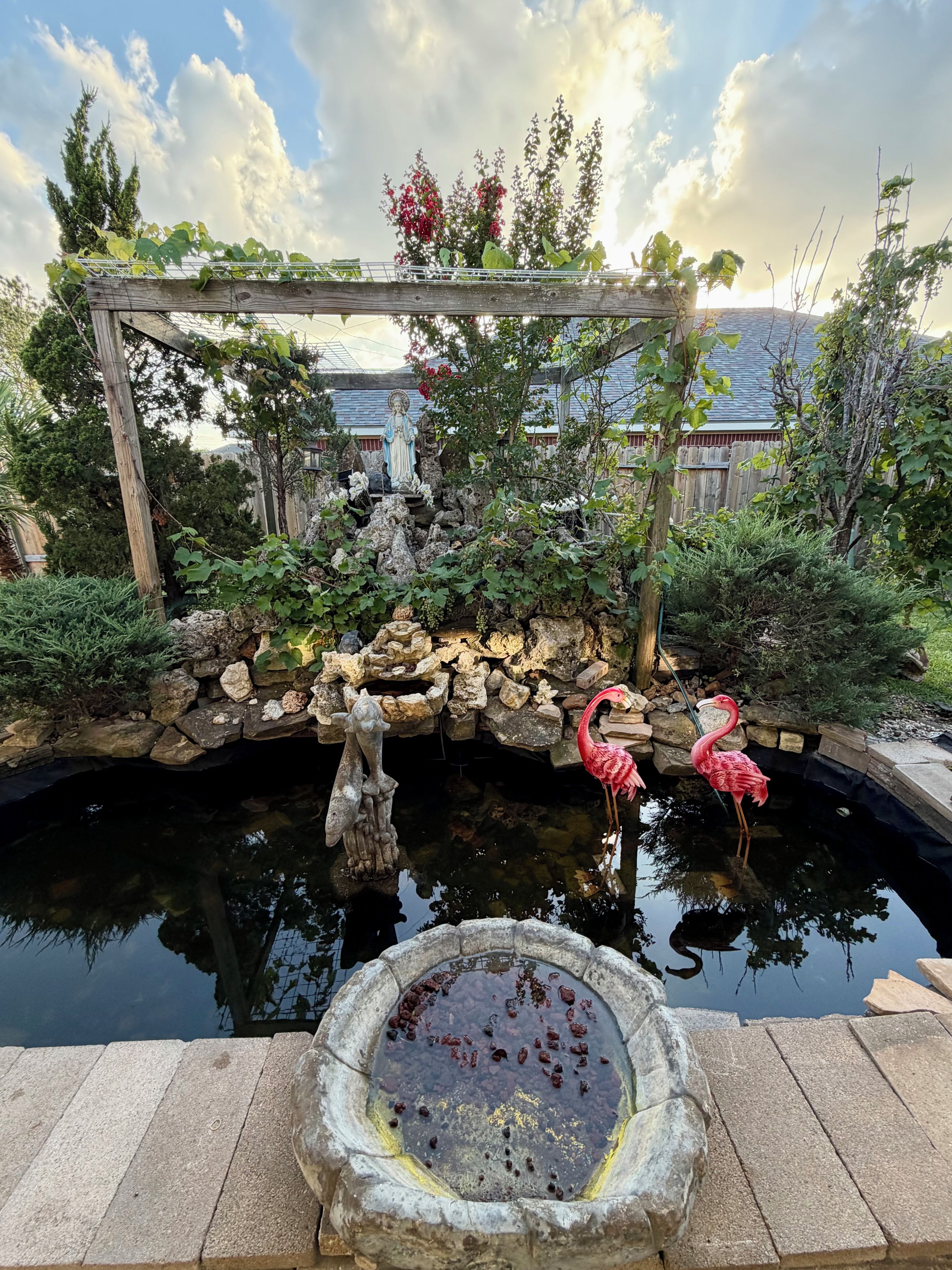 A garden with a pond, a statue, and two flamingos.