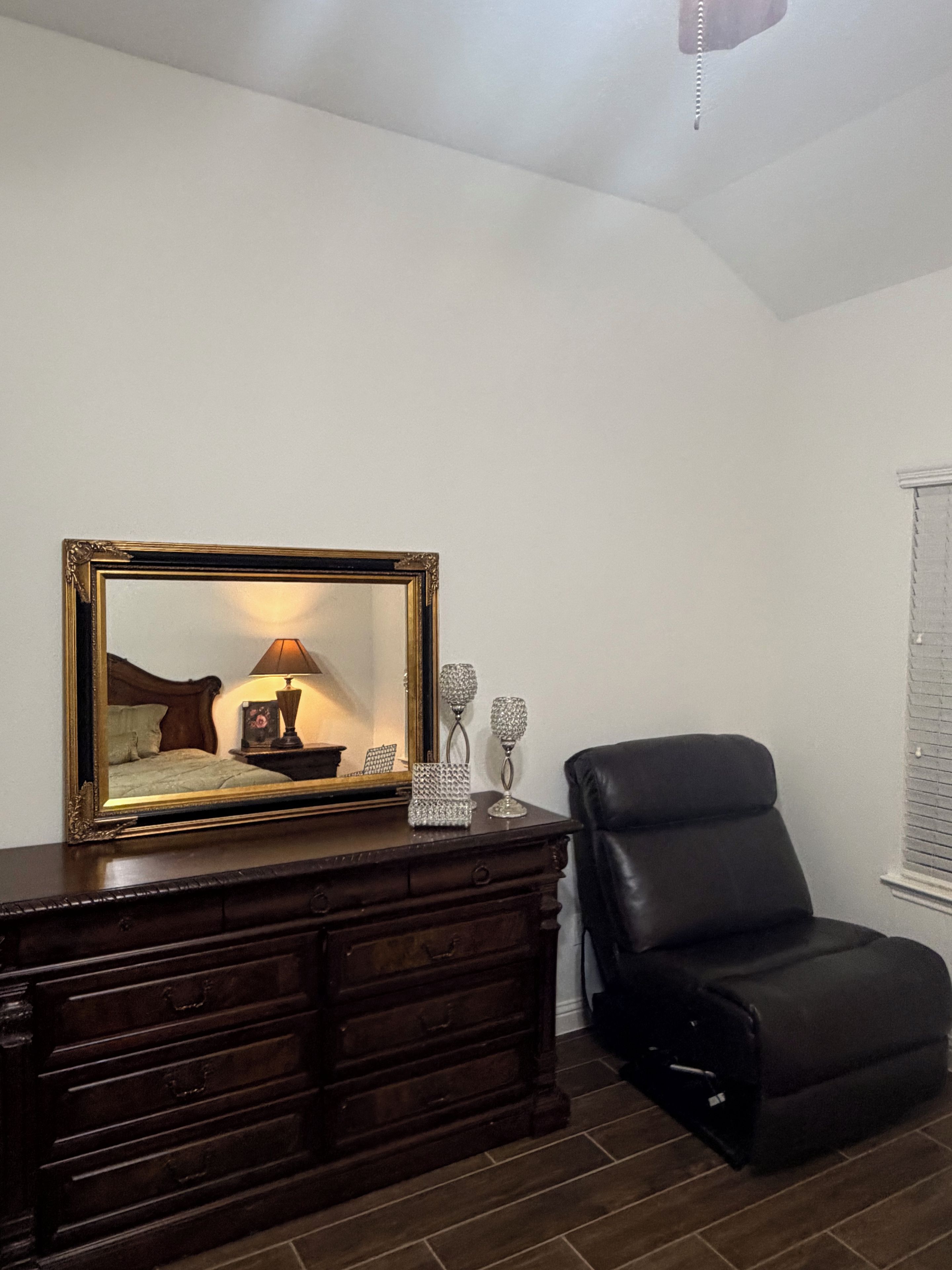 A room with a wooden dresser, a mirror, a lamp, and a black leather chair.