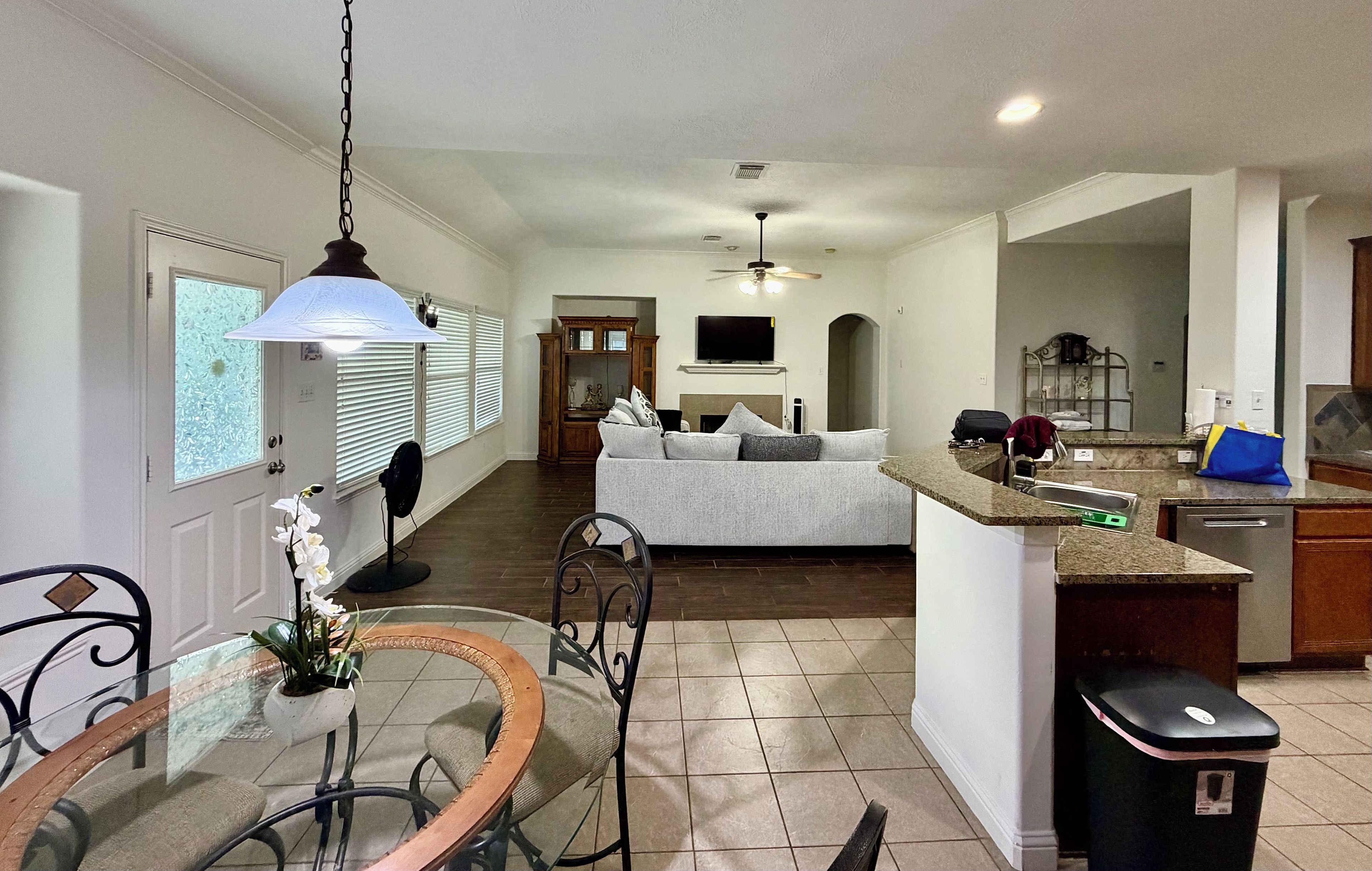 A modern kitchen with a dining area, a living room with a sofa, and a TV mounted on the wall.