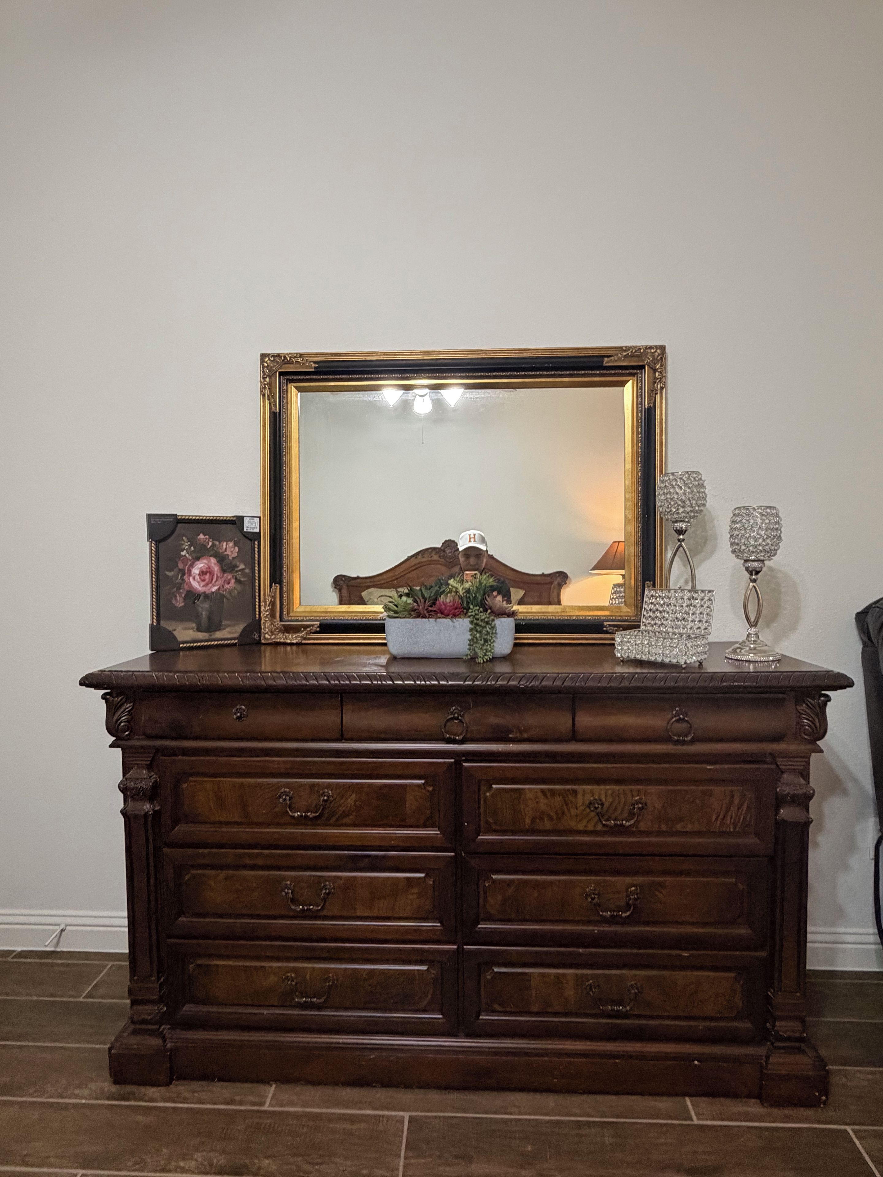 Een houten dressoir met een grote spiegel, een lijst met een afbeelding en decoratieve objecten.
